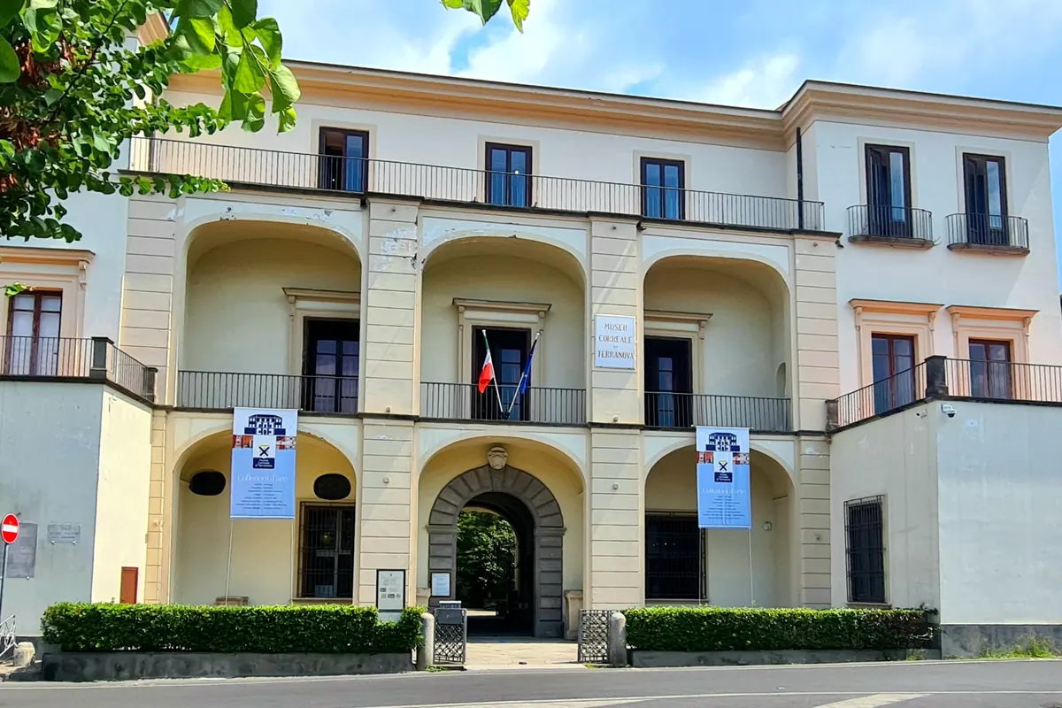 The cream-coloured front of the Museo Correale di Terranova in Sorrento, with three arched loggias above a stone gateway, iron-railed balconies and a leafy branch in the corner.